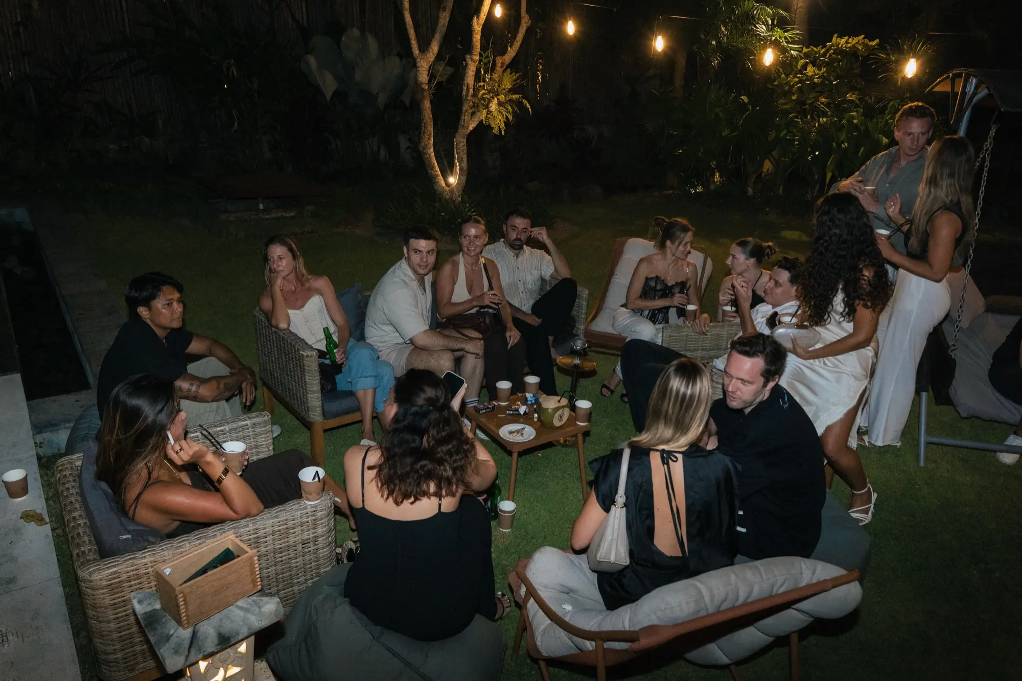 Guests sitting and talking on the lawn at night, under string lights